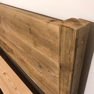 Op de afbeelding: Een hoofdeinde opgebouwd uit horizontale lichtbruine houten planken met een zichtbare houtnerf. De structuur is voorzien van een dikke, verticale houten paal aan de rechterkant, vastgezet met ronde houten deuvels langs de zijkant.
