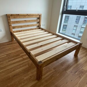 May include: A wooden bed frame with a slatted headboard and footboard. The frame is made of natural wood with a rustic finish. The bed is sitting on a wooden floor.