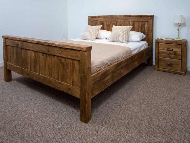 Puede incluir: Un marco de cama de madera r&uacute;stica con una cabecera y un piecero de listones. La cama est&aacute; hecha de madera recuperada y tiene un acabado marr&oacute;n natural. La cama est&aacute; vestida con un edred&oacute;n beige y almohadas.