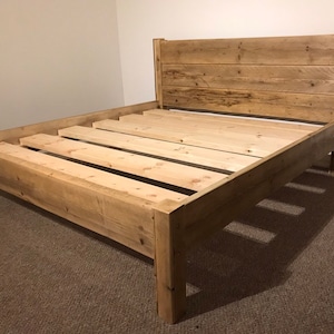 May include: A wooden bed frame with a natural finish. The frame has a headboard and footboard, and is supported by slats.