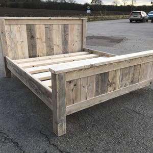 May include: A wooden bed frame made from reclaimed timber. The headboard and footboard are constructed from vertical planks of varying widths. The bed frame is made of light-coloured wood, with visible grain and knots, giving it a natural, weathered appearance.