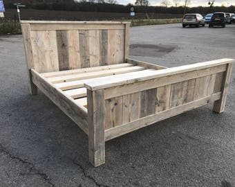 Puede incluir: Un armazón de cama de madera rústica sin terminar. El cabecero y el pie de cama están construidos con tablones verticales de diferentes anchos. El armazón de la cama es de madera de color claro, con vetas y nudos visibles, lo que le da un aspecto natural y envejecido.