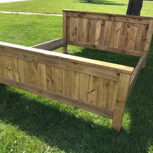 Puede incluir: Un marco de cama de madera con un acabado de madera natural. La cabecera y el piecero est&aacute;n hechos de anchas tablas de madera.