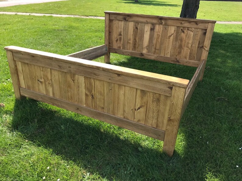 Puede incluir: Un marco de cama de madera con un acabado de madera natural. La cabecera y el piecero est&aacute;n hechos de anchas tablas de madera.