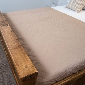 Puede incluir: Un cabecero de cama de madera con un edred&oacute;n acolchado de color marr&oacute;n claro. El cabecero de cama est&aacute; hecho de madera reciclada y tiene un aspecto r&uacute;stico.