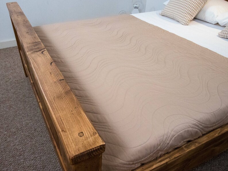 Puede incluir: Un cabecero de cama de madera con un edred&oacute;n acolchado de color marr&oacute;n claro. El cabecero de cama est&aacute; hecho de madera reciclada y tiene un aspecto r&uacute;stico.