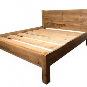 Op de afbeelding: Een houten bedframe met een hoog hoofdeinde opgebouwd uit horizontale planken en een stevige basis met dikke hoekpalen. Het frame bevat een reeks lichtgekleurde houten latten in het midden om een matras te ondersteunen.