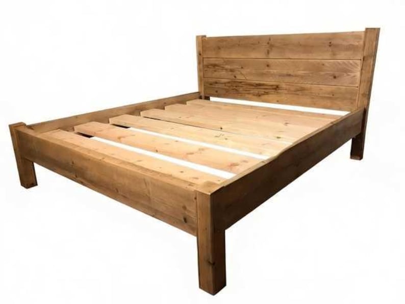 Op de afbeelding: Een houten bedframe met een hoog hoofdeinde opgebouwd uit horizontale planken en een stevige basis met dikke hoekpalen. Het frame bevat een reeks lichtgekleurde houten latten in het midden om een matras te ondersteunen.