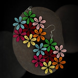 May include: Colorful flower earrings with a black outline. The earrings feature a variety of colors, including red, pink, yellow, green, and blue. The earrings are made of paper and have silver hooks.