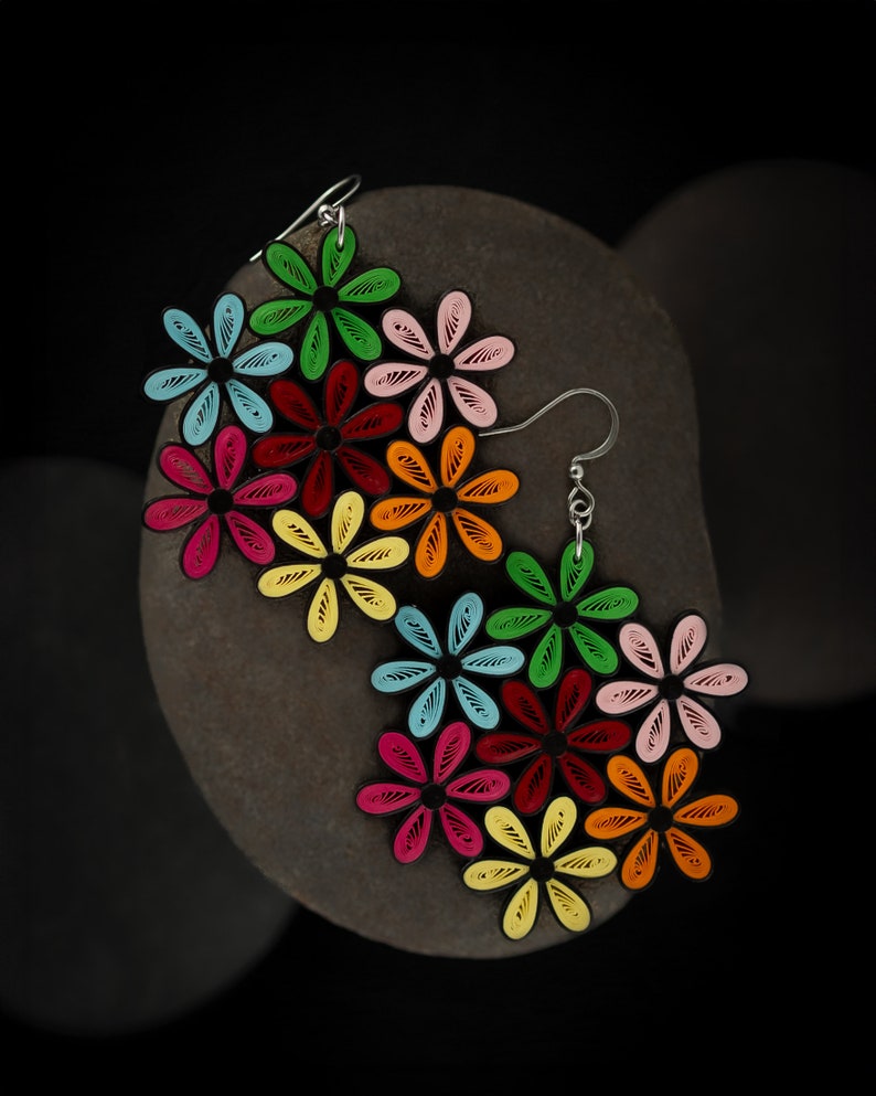 May include: Colorful flower earrings with a black outline. The earrings feature a variety of colors, including red, pink, yellow, green, and blue. The earrings are made of paper and have silver hooks.