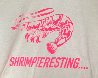 May include: A white t-shirt with a pink shrimp design and the text "Shrimpteresting..." printed on the front.