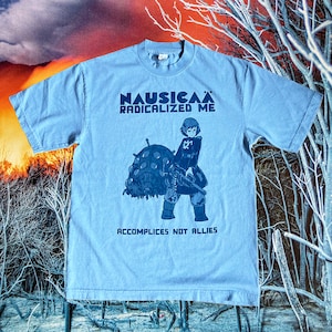 Puede incluir: Una camiseta azul claro con un estampado gr&aacute;fico de un personaje de la pel&iacute;cula de anime "Nausica&auml; del Valle del Viento". El texto "Nausica&auml; Radicalized Me" y "Accomplices Not Allies" est&aacute; impreso en la camiseta.