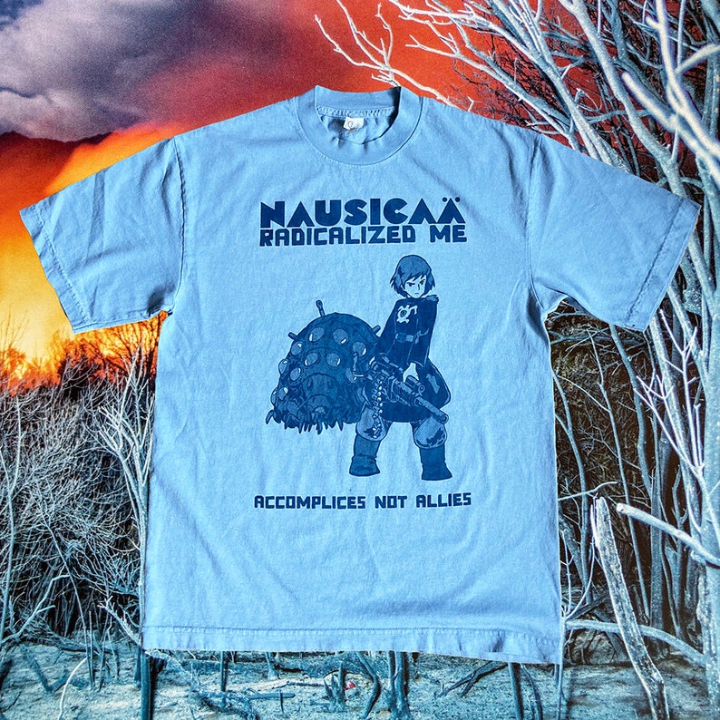 Puede incluir: Una camiseta azul claro con un estampado gr&aacute;fico de un personaje de la pel&iacute;cula de anime "Nausica&auml; del Valle del Viento". El texto "Nausica&auml; Radicalized Me" y "Accomplices Not Allies" est&aacute; impreso en la camiseta.