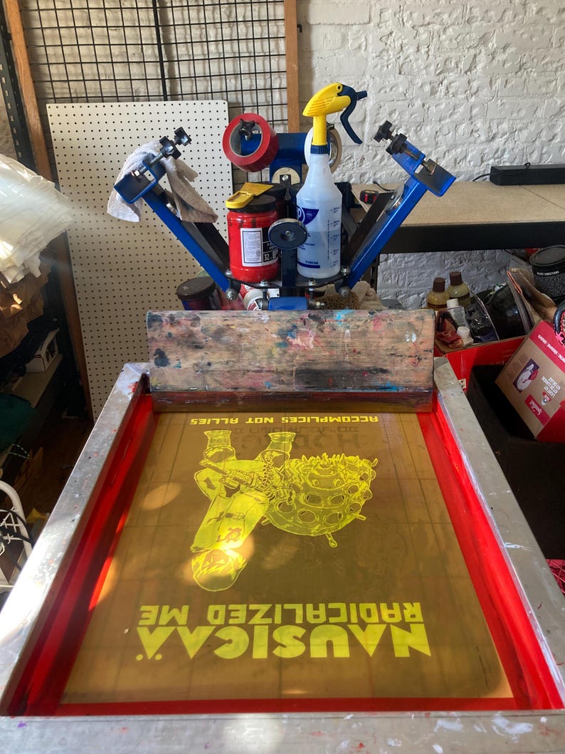 Puede incluir: Un marco de serigraf&iacute;a amarillo con un dise&ntilde;o de una persona sosteniendo una esfera grande con el texto "MUSIC.A RADICALIZED ME. ACCOMPLICES NOT ALLIES." impreso en &eacute;l.