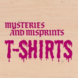 May include: Pink graphic text on a wood background that reads "mysteries and misprints T-SHIRTS".