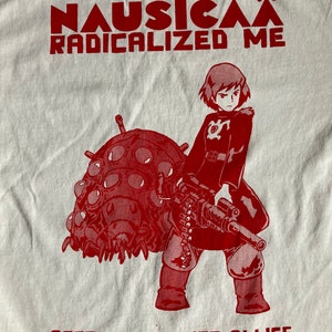 Puede incluir: Impresi&oacute;n gr&aacute;fica roja en una camiseta blanca con un personaje de la pel&iacute;cula de anime Nausica&auml; del Valle del Viento. El texto dice "Nausica&auml; Radicalized Me" y "Accomplices Not Allies".