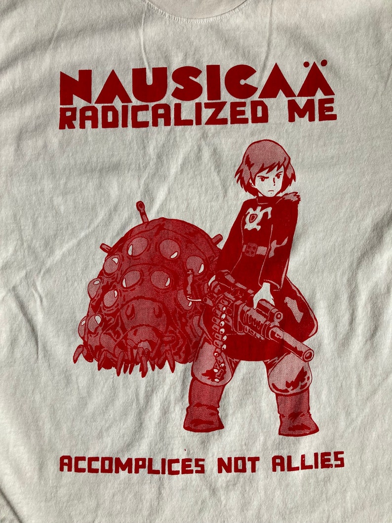 Puede incluir: Impresi&oacute;n gr&aacute;fica roja en una camiseta blanca con un personaje de la pel&iacute;cula de anime Nausica&auml; del Valle del Viento. El texto dice "Nausica&auml; Radicalized Me" y "Accomplices Not Allies".