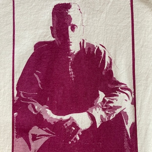 Puede incluir: Una camiseta vintage con una imagen en color burdeos de una persona sentada con las manos juntas. El texto de la camiseta dice "INSTITUTIONALIZED BIGOTRY AND OPPRESSION AROSE WITH THE DIVISION OF SOCIETY INTO EXPLOITER AND EXPLOITED. DIVIDE-AND-CONQUER TACTICS"