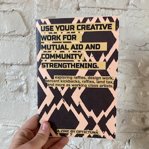 Op de afbeelding: Een zwart en perzikkleurig zine met de tekst "USE YOUR CREATIVE WORK FOR MUTUAL AID AND COMMUNITY STRENGTHENING." Het zine heeft een geometrisch patroon en de tekst is in goud. De tekst onder de titel luidt: "exploring raffles, design work, percent kickbacks, raffles, land tax, and more as working class artists." Onderaan het zine staat "A ZINE BY OPTICTUNA."