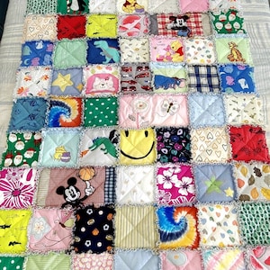 K&ouml;nnte beinhalten: Eine bunte Patchwork-Decke aus Stoffquadraten mit verschiedenen Comicfiguren, Tieren und Mustern. Die Decke ist in verschiedenen Farben gehalten, darunter Rot, Blau, Gr&uuml;n, Gelb und Pink.