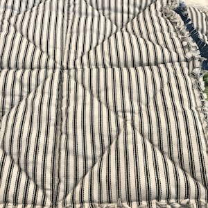 K&ouml;nnte beinhalten: Ein wei&szlig;-schwarz gestreiftes Stoff mit einer gesteppten Textur. Der Stoff hat einen ausgefransten Rand.