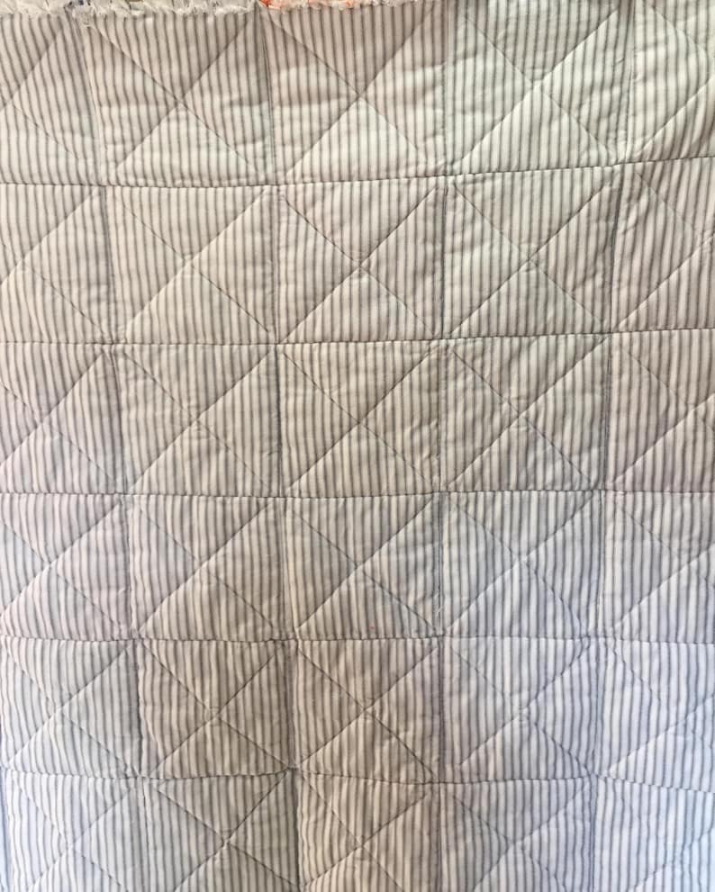 K&ouml;nnte beinhalten: Eine wei&szlig;e und graue gestreifte Steppdecke mit einem Rautenmuster. Die Steppdecke ist mit einem einfachen Stich gesteppt.
