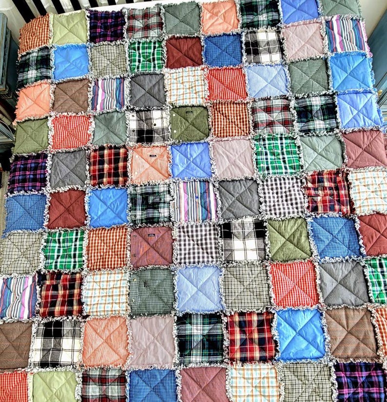 K&ouml;nnte beinhalten: Eine Patchwork-Decke aus Quadraten aus verschiedenen karierten Stoffen in Blaut&ouml;nen, Gr&uuml;n, Rot, Braun und Wei&szlig;. Die Decke ist mit einer ausgefransten Kanten-Technik gefertigt, was ihr einen rustikalen Look verleiht.
