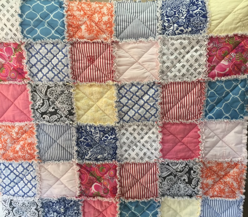 K&ouml;nnte beinhalten: Eine Patchwork-Decke mit einer Vielzahl von bunten Stoffen, darunter Rosa, Blau, Rot, Gelb und Orange. Die Decke besteht aus Quadraten und hat einen gekr&auml;uselten Rand.
