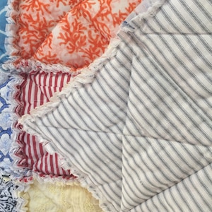 K&ouml;nnte beinhalten: Eine Patchwork-Decke aus verschiedenen Stoffen mit einer Vielzahl von Mustern, darunter Streifen, Blumen und geometrische Muster. Die Decke ist mit einem ausgefransten Rand gefertigt und hat einen rustikalen, handgefertigten Look.