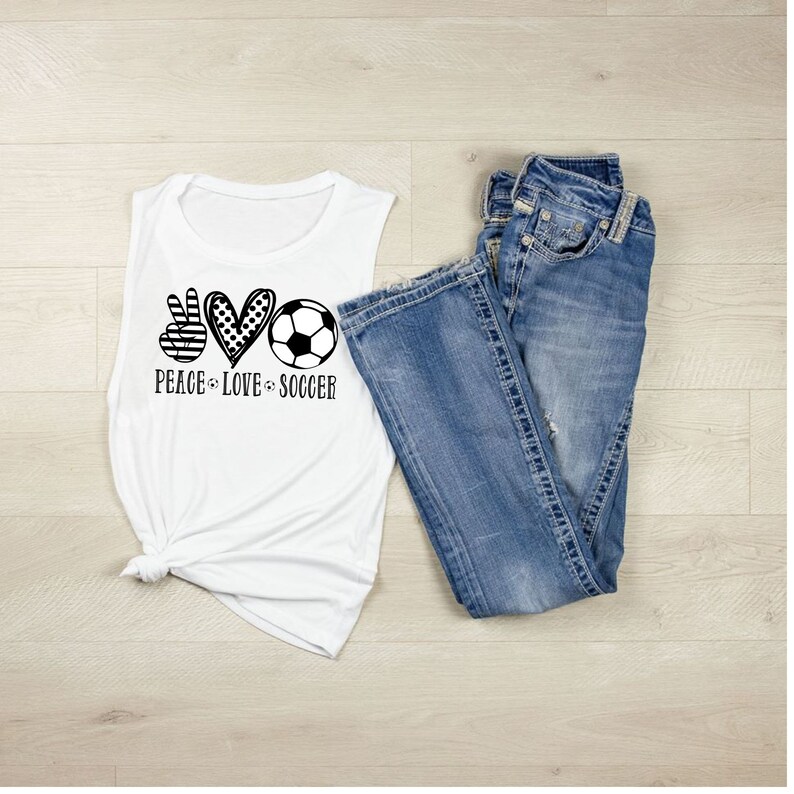 May include: White sleeveless muscle tank top with a black and white graphic of a peace sign, heart, and soccer ball. The text "Peace Love Soccer" is below the graphic.