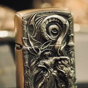 May include: A silver lighter with an intricate, detailed design featuring a winged figure and a dragon. The design is embossed and has a three-dimensional effect.