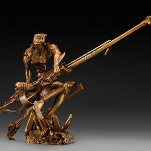 Puede incluir: Una estatua de bronce de un robot sosteniendo una gran arma. El robot está de pie sobre una base rocosa. La estatua es un artículo de colección.