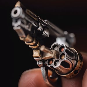 May include: A close-up of a small, silver revolver with a brass cylinder. The cylinder is open, revealing six empty chambers.