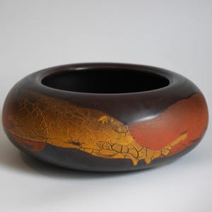 May include: A brown ceramic bowl with a wide, rounded shape. The exterior features a textured, crackled design in shades of gold and orange, contrasting with the dark brown base and interior. The bowl is designed for decorative purposes.