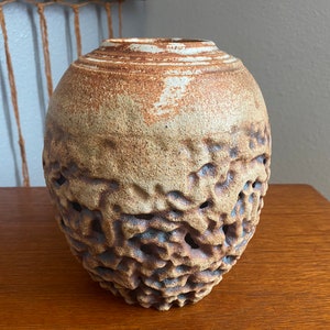 May include: A brown and white ceramic vase with a textured, honeycomb-like design. The vase has a round body and a wide opening.