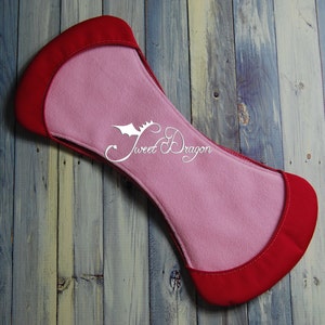 May include: A red and pink fabric pad with a curved shape and a white logo that says "Sweet Dragon".