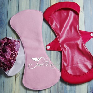 May include: Two reusable cloth pads, one pink and one red, with a third cloth pad with a pink and purple patterned design. The pads are made of soft, absorbent fabric and are designed to be used as an alternative to disposable sanitary pads.