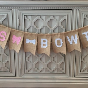 May include: A burlap banner with the words "Bow Ties" in white letters. The banner is decorated with a pink bow and a white bow tie.