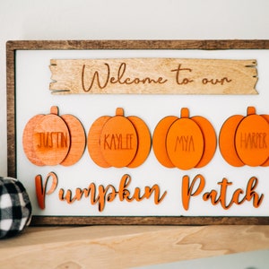May include: Welcome to our Pumpkin Patch sign with four orange pumpkin cutouts with names Justin, Kaylie, Mya, and Harper. The sign is framed in brown wood and has a small black and white plaid pumpkin in the bottom left corner.