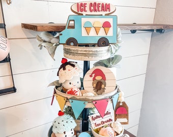May include: A three-tiered tiered tray decorated with a blue ice cream truck, ice cream cones, a gnome, and a crocheted ice cream cone. The tray is decorated with a banner that says "Hello and Ice Cream".