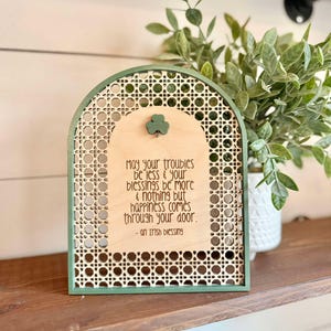 Irish Blessing Sign by Walnut + Birch. Irish Blessing reads "May your troubles be less & and your blessings be more & nothing but happiness comes through your door". Rattan oval shaped sign with green frame and 3 leaf clover.