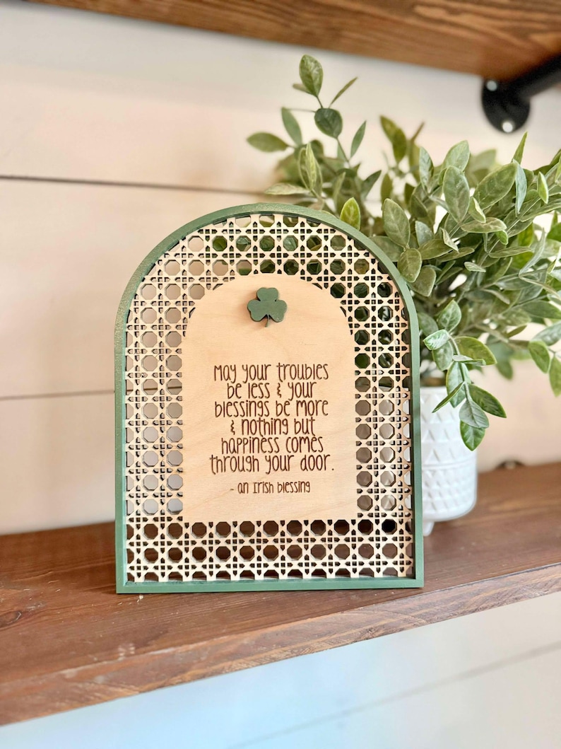 Irish Blessing Sign by Walnut + Birch. Irish Blessing reads "May your troubles be less & and your blessings be more & nothing but happiness comes through your door". Rattan oval shaped sign with green frame and 3 leaf clover.