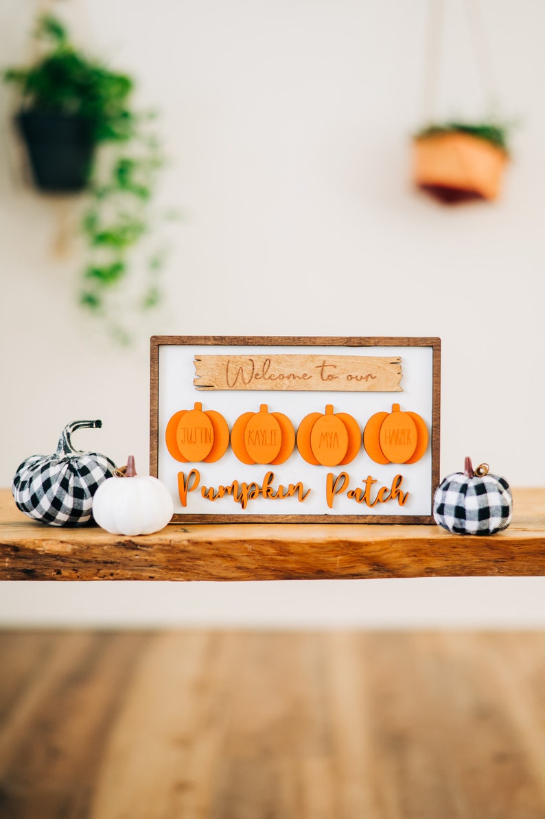 May include: Welcome to our Pumpkin Patch sign with four orange pumpkin-shaped ornaments with names on them. The sign is on a wooden table with two small decorative pumpkins.