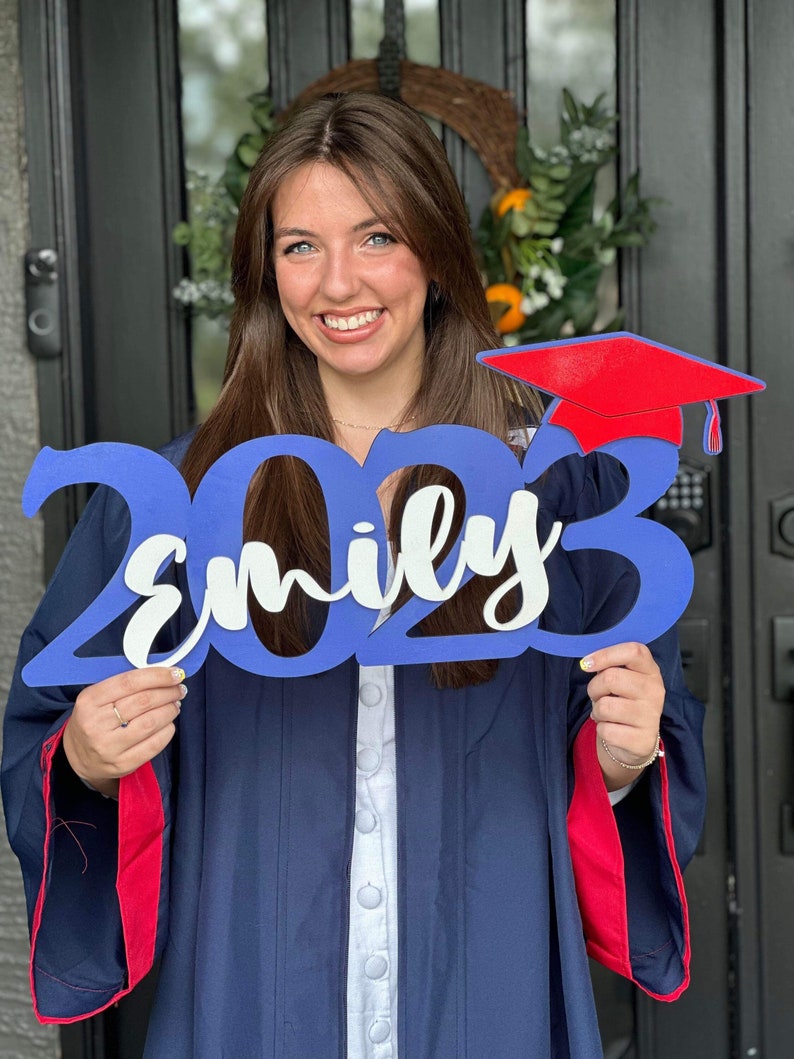 Grad Sign shown with 2023 with the 2023 in Royal Blue, The Hat in Red and the name in white by walnut + birch