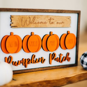 May include: A wooden sign with the text "Welcome to our Pumpkin Patch" and four orange pumpkin-shaped ornaments with the names "Justin", "Kylie", "Mya", and "Abby" written on them.