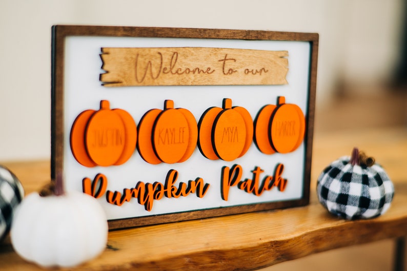 May include: A wooden sign with the text "Welcome to our Pumpkin Patch" and four orange pumpkin-shaped ornaments with the names "Justin", "Kylie", "Mya", and "Abby" written on them.