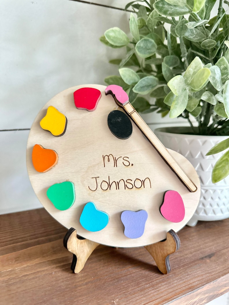 May include: Wooden paint palette with colourful paint drops and a paintbrush, personalised with the name "mrs. Johnson".