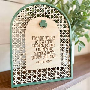 Irish Blessing Sign by Walnut + Birch. Irish Blessing reads "May your troubles be less & and your blessings be more & nothing but happiness comes through your door". Rattan oval shaped sign with green frame and 3 leaf clover.