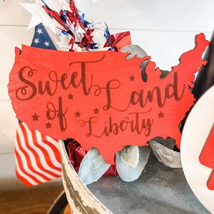 Puede incluir: Corte de madera rojo en forma de los Estados Unidos con el texto "Sweet Land of Liberty" en letras marrones.