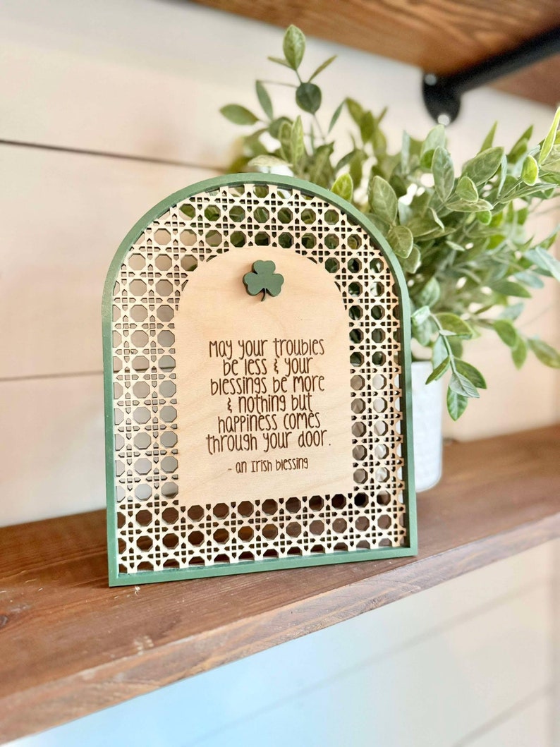 Irish Blessing Sign by Walnut + Birch. Irish Blessing reads "May your troubles be less & and your blessings be more & nothing but happiness comes through your door". Rattan oval shaped sign with green frame and 3 leaf clover.